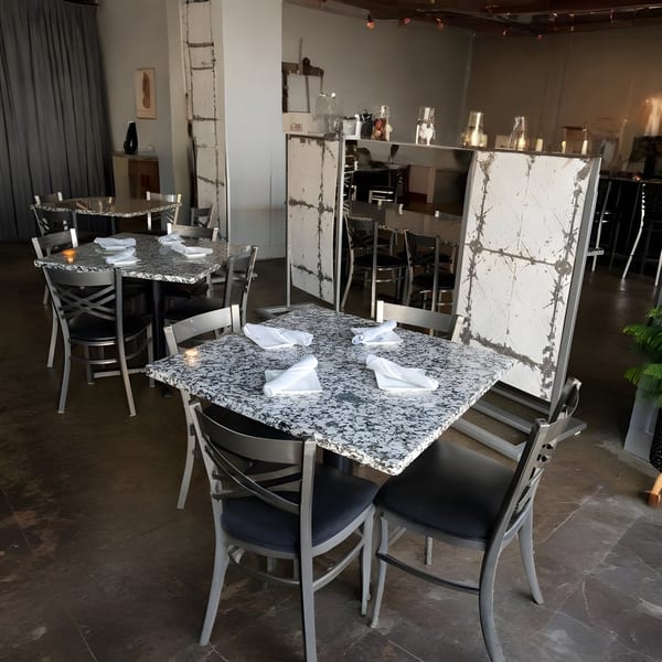 Alma Kitchen dining room with granite tables, metal chairs, and white dividers creating an industrial ambiance.