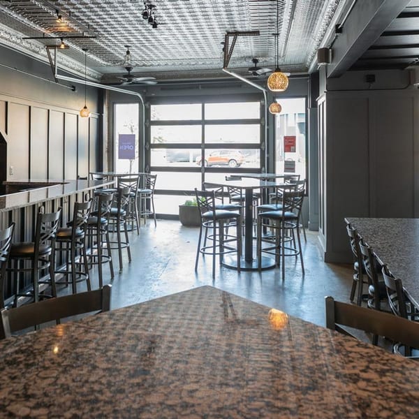 Interior of Alma Kitchen with high-top tables, bar seating, and a large glass garage door.
