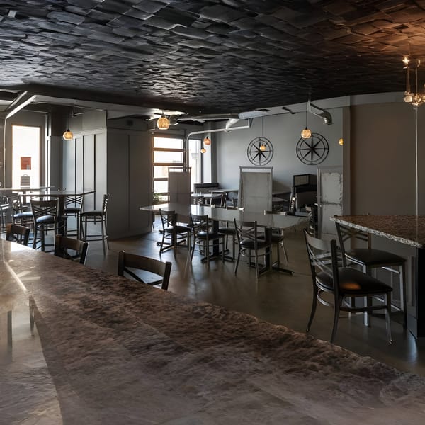 The Alma Kitchen dining area features dark tables, chairs, and a textured ceiling with warm lighting.
