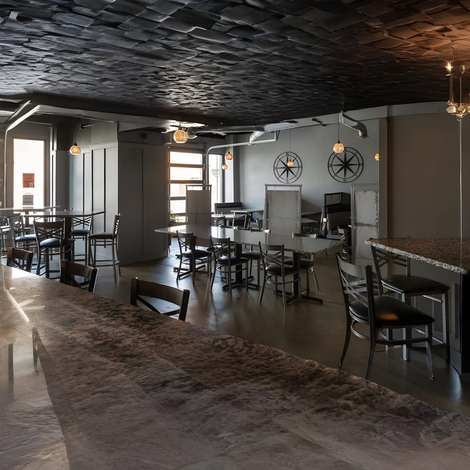 The Alma Kitchen dining area features dark tables, chairs, and a textured ceiling with warm lighting.