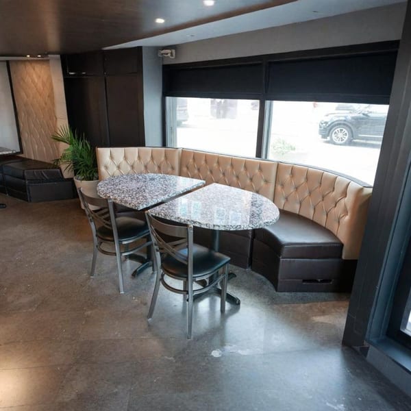 Alma Kitchen's dining area features a curved booth with two granite tables and chairs by a window.