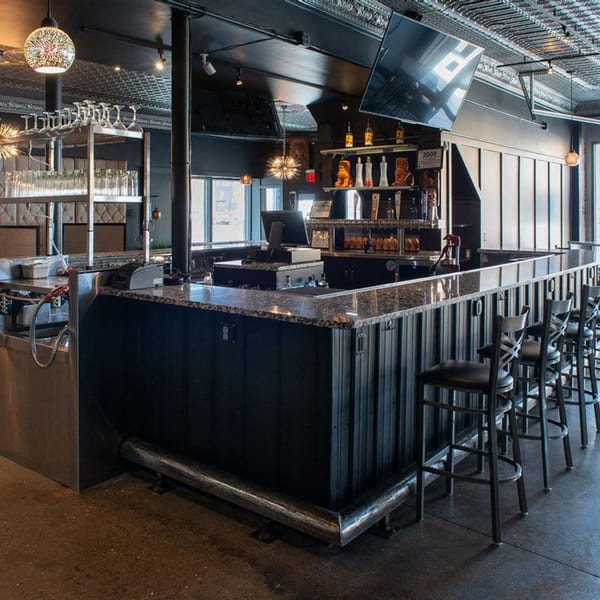A modern, dark-themed bar area at Alma Kitchen with granite countertops and bar stools.