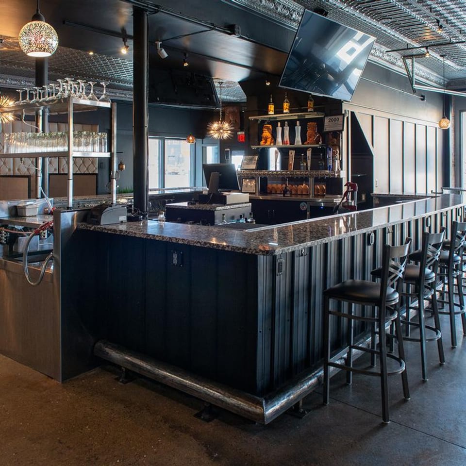 A modern, dark-themed bar area at Alma Kitchen with granite countertops and bar stools.
