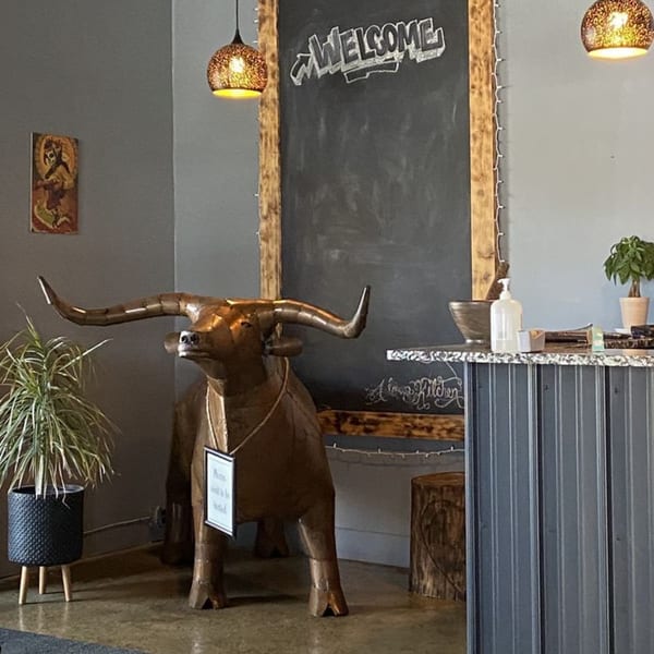 A large bronze bull statue stands near a chalkboard with "WELCOME" written on it at Alma Kitchen.