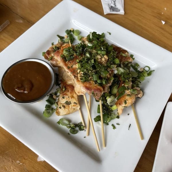 Chicken skewers topped with green onions and peanuts, served with a side of peanut sauce.