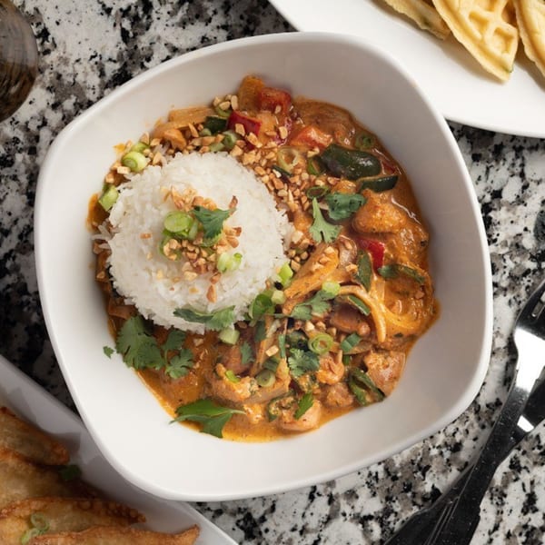 A white bowl of Alma Kitchen's American curry with rice, peanuts, and cilantro on a granite counter.