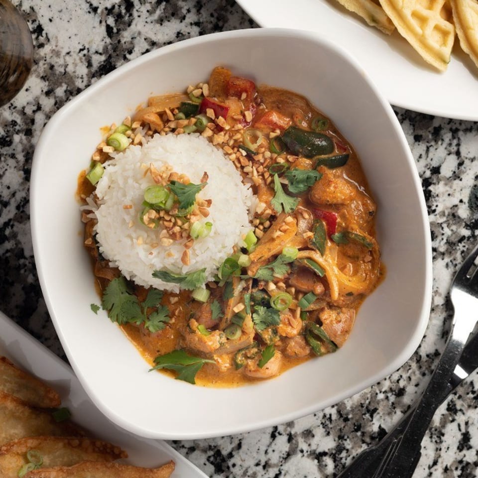 A white bowl of Alma Kitchen's American curry with rice, peanuts, and cilantro on a granite counter.