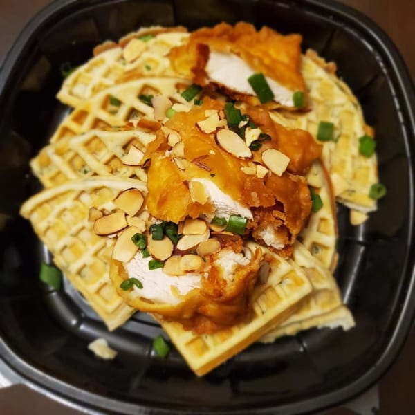 Alma Kitchen's chicken and waffles, topped with sliced almonds and green onions in a black bowl.