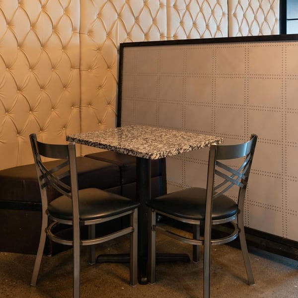 A cozy Alma Kitchen dining nook with a granite table, two chairs, and tufted booth seating.
