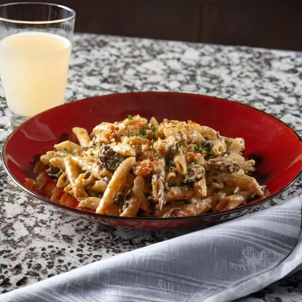 Creamy penne pasta with mushrooms and breadcrumbs in a red bowl, with a drink and napkin.