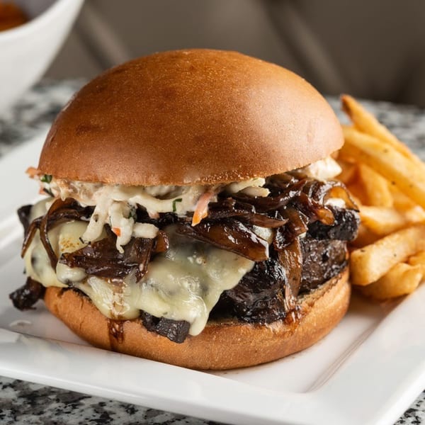 Alma Kitchen's American burger with melted cheese, caramelized onions, coleslaw, and a side of fries.