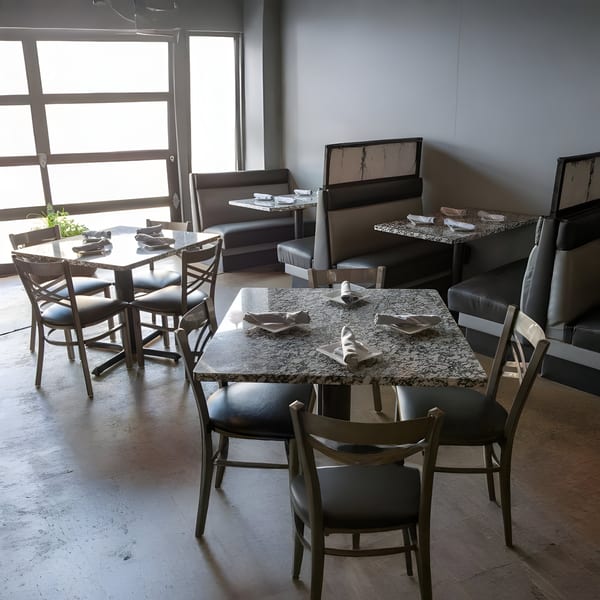 Alma Kitchen's dining room with granite tables, black chairs, and booths, illuminated by large windows.